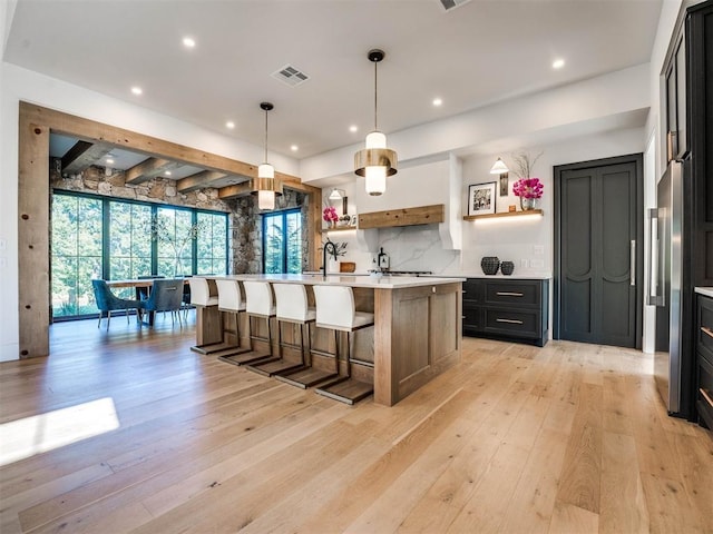 kitchen featuring high end fridge, tasteful backsplash, light hardwood / wood-style flooring, an island with sink, and pendant lighting