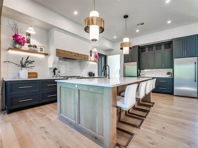 kitchen with stainless steel appliances, decorative light fixtures, light hardwood / wood-style flooring, and a large island with sink