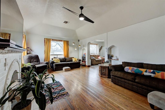 living room with lofted ceiling, a brick fireplace, wood-type flooring, and ceiling fan