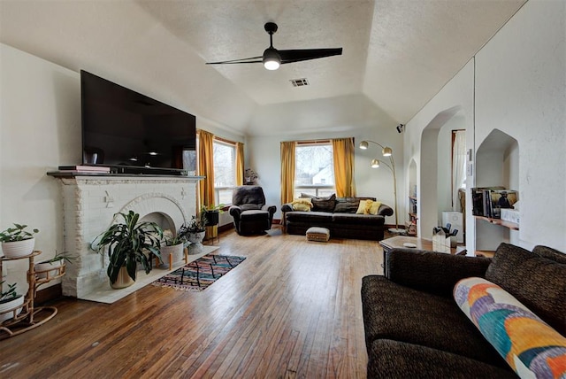 living room featuring a brick fireplace, a tray ceiling, wood-type flooring, and ceiling fan