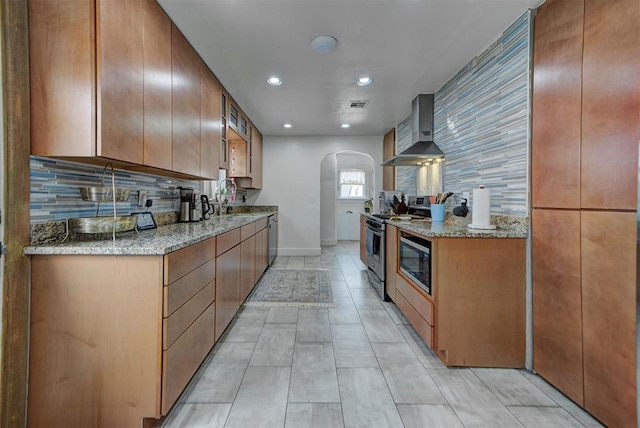 kitchen featuring stainless steel appliances, tasteful backsplash, wall chimney range hood, and light stone counters