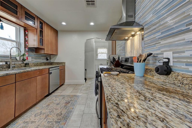 kitchen featuring wall chimney exhaust hood, tasteful backsplash, light stone counters, appliances with stainless steel finishes, and a healthy amount of sunlight