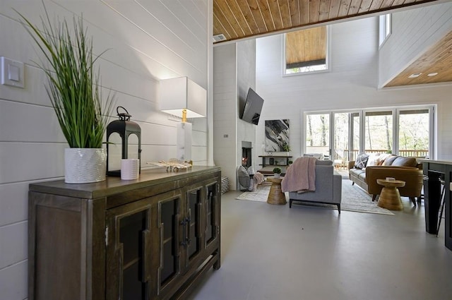 living room with a towering ceiling, concrete flooring, a large fireplace, and wooden ceiling