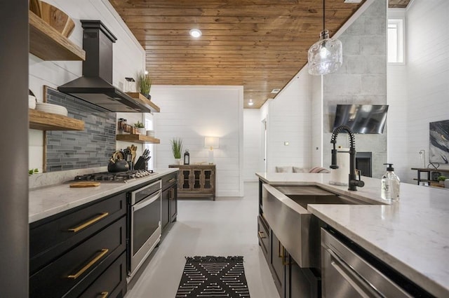 kitchen featuring pendant lighting, wall chimney range hood, light stone counters, and stainless steel appliances