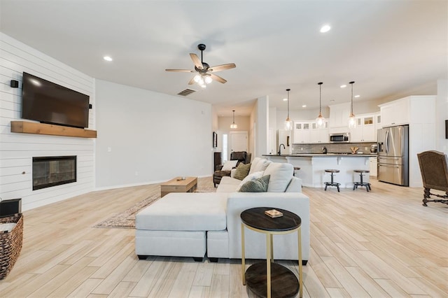 living room featuring ceiling fan, a large fireplace, and light hardwood / wood-style floors