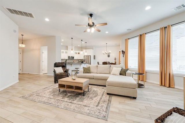 living room featuring ceiling fan with notable chandelier and light hardwood / wood-style flooring