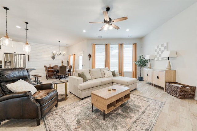 living room featuring ceiling fan with notable chandelier and light hardwood / wood-style flooring