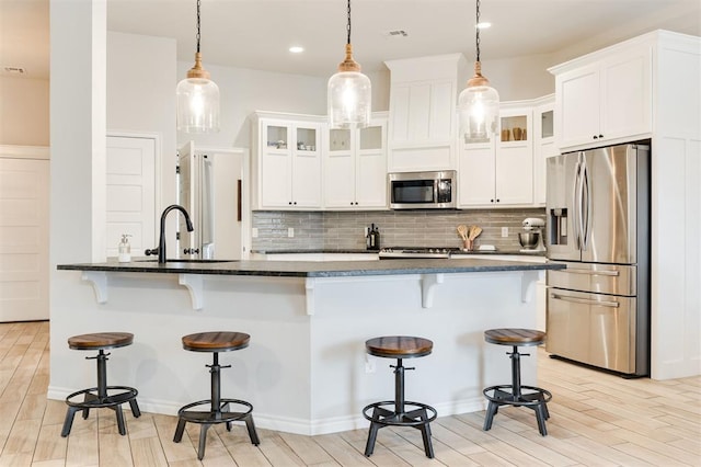 kitchen with white cabinetry, stainless steel appliances, decorative light fixtures, and a breakfast bar area