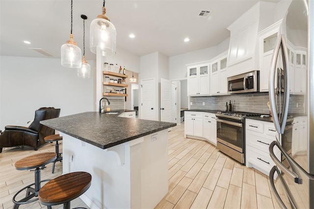 kitchen featuring appliances with stainless steel finishes, a breakfast bar, decorative light fixtures, white cabinetry, and sink