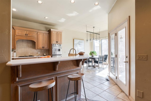 kitchen featuring backsplash, a kitchen bar, hanging light fixtures, light tile patterned floors, and stainless steel double oven