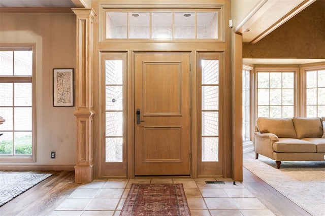 foyer entrance featuring decorative columns, light tile patterned flooring, and ornamental molding