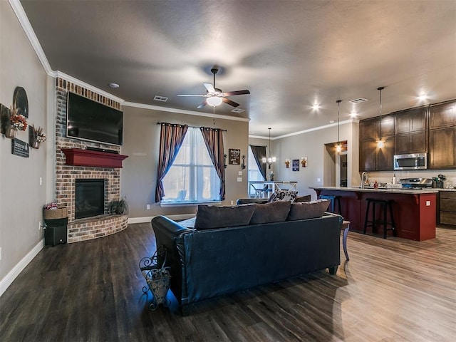 living room featuring ornamental molding, a brick fireplace, dark hardwood / wood-style floors, and ceiling fan with notable chandelier