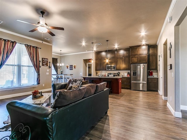 living room with dark wood-type flooring, ornamental molding, and ceiling fan with notable chandelier