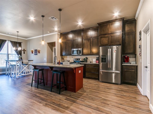 kitchen with pendant lighting, a breakfast bar, a kitchen island with sink, stainless steel appliances, and light stone counters