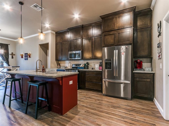 kitchen with a center island with sink, appliances with stainless steel finishes, a kitchen breakfast bar, pendant lighting, and light stone countertops