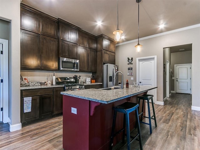 kitchen with sink, hanging light fixtures, a kitchen island with sink, stainless steel appliances, and dark brown cabinets