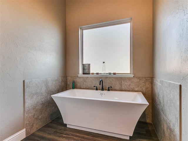 bathroom featuring wood-type flooring, tile walls, and a washtub