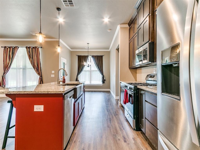 9015 Tall Oaks Dr, Guthrie, OK 73044 - kitchen featuring stainless steel appliances, ornamental molding, light wood-style flooring, a center island with sink, and a breakfast bar