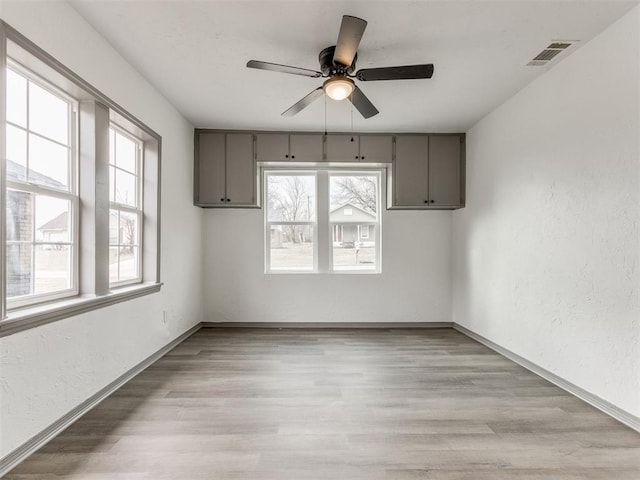 empty room with ceiling fan, a healthy amount of sunlight, and light hardwood / wood-style flooring