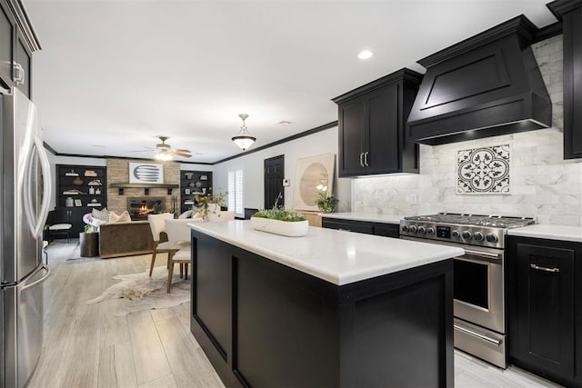 kitchen featuring premium range hood, crown molding, a large fireplace, appliances with stainless steel finishes, and a kitchen island