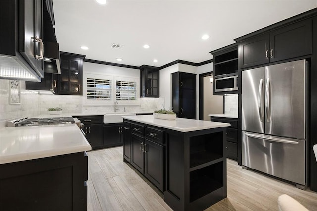 kitchen featuring a kitchen island, appliances with stainless steel finishes, decorative backsplash, light hardwood / wood-style floors, and crown molding