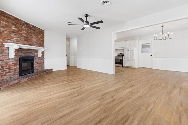 unfurnished living room featuring ceiling fan with notable chandelier, a fireplace, and light wood-type flooring