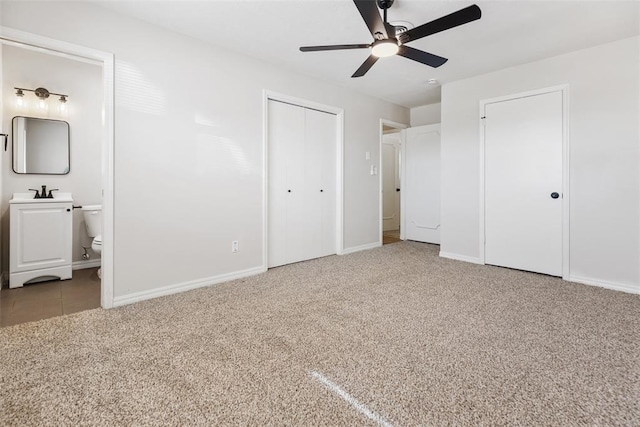 unfurnished bedroom with sink, ensuite bath, ceiling fan, carpet floors, and two closets