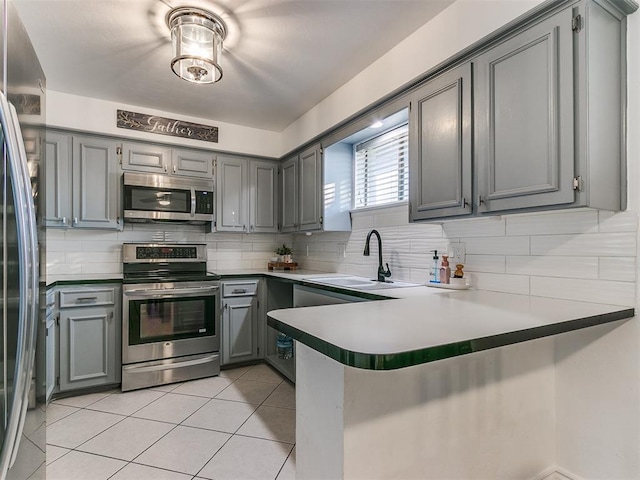 kitchen featuring sink, gray cabinets, stainless steel appliances, light tile patterned flooring, and kitchen peninsula