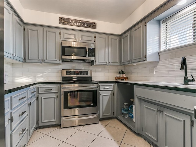 kitchen featuring gray cabinetry, sink, light tile patterned floors, and appliances with stainless steel finishes