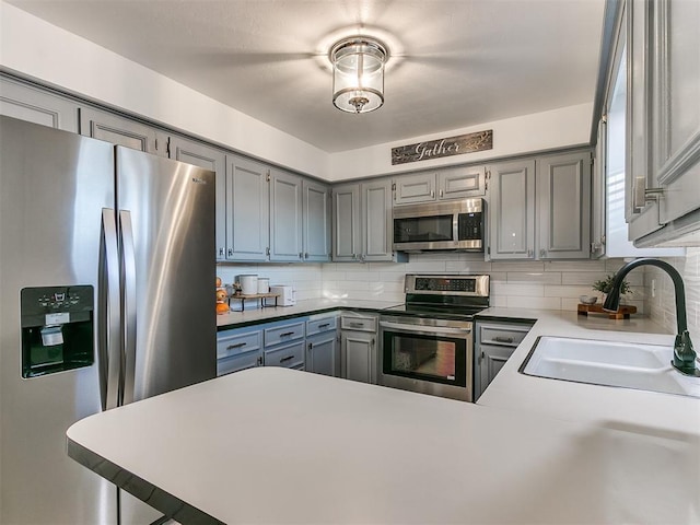 kitchen featuring stainless steel appliances, gray cabinets, sink, and backsplash