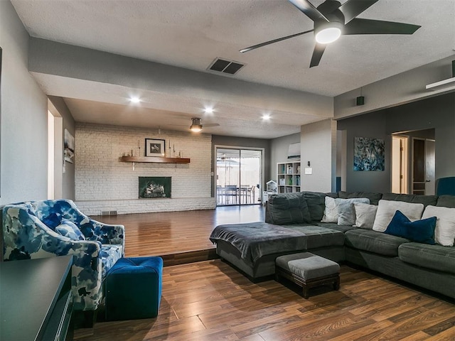 living room with ceiling fan, dark hardwood / wood-style floors, a fireplace, a textured ceiling, and brick wall