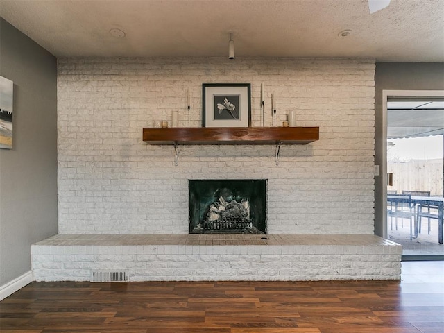 unfurnished living room with dark hardwood / wood-style flooring, a brick fireplace, and a textured ceiling