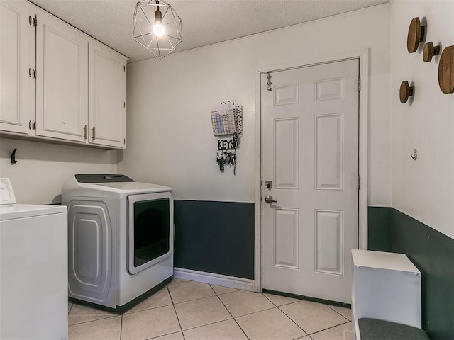 laundry area featuring light tile patterned floors, washing machine and dryer, cabinets, and a textured ceiling