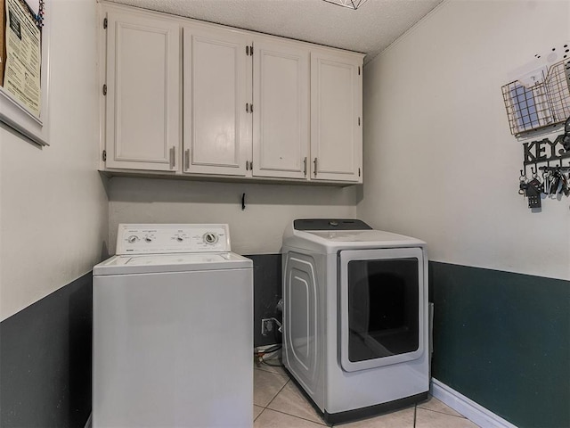 clothes washing area with cabinets, separate washer and dryer, a textured ceiling, and light tile patterned floors