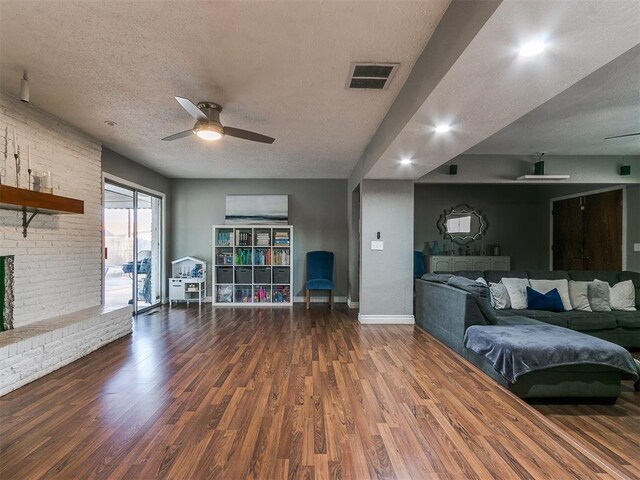 living room with ceiling fan, a textured ceiling, dark hardwood / wood-style flooring, and a fireplace