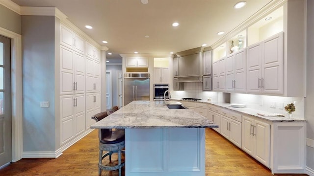 kitchen featuring light stone counters, stainless steel appliances, white cabinets, and a center island with sink