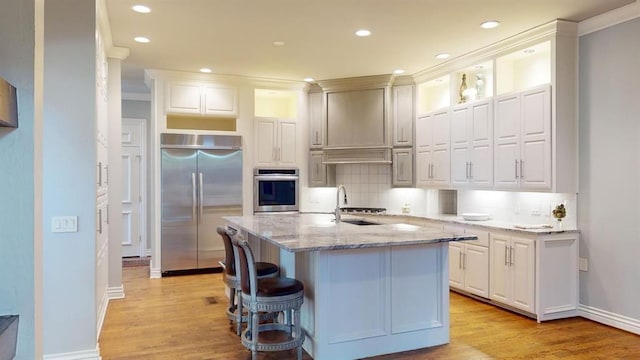 kitchen featuring sink, white cabinetry, light stone counters, a center island with sink, and stainless steel appliances