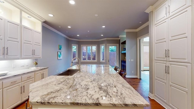 kitchen with white cabinetry, light stone countertops, a kitchen island with sink, and sink