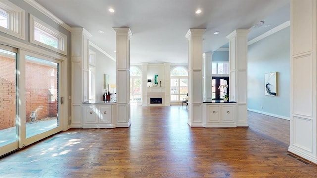 unfurnished living room with ornate columns, crown molding, and dark wood-type flooring