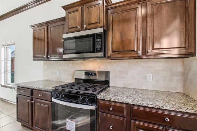 kitchen with light tile patterned floors, crown molding, appliances with stainless steel finishes, backsplash, and light stone countertops