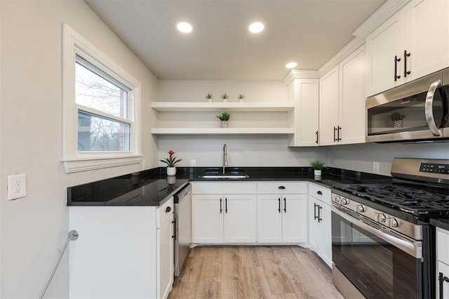 kitchen with sink, white cabinetry, light hardwood / wood-style flooring, dark stone countertops, and stainless steel appliances