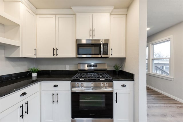 kitchen featuring stainless steel appliances, dark stone counters, white cabinets, and light wood-type flooring