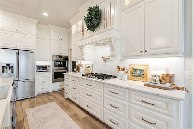 kitchen featuring stainless steel appliances, white cabinets, light wood finished floors, and tasteful backsplash