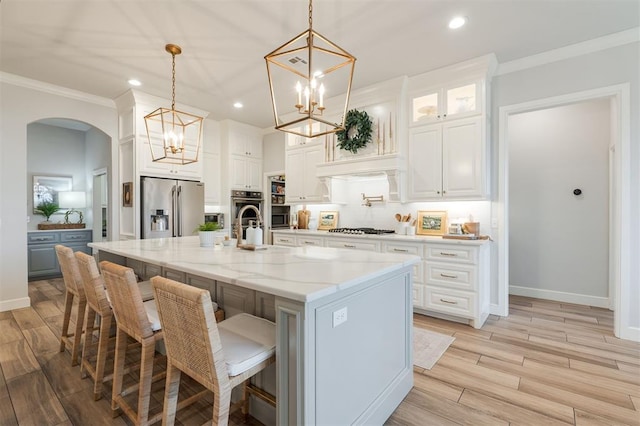 kitchen with light wood-style floors, ornamental molding, stainless steel appliances, and arched walkways