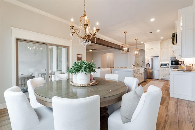 dining room with light wood-type flooring, arched walkways, a chandelier, and crown molding