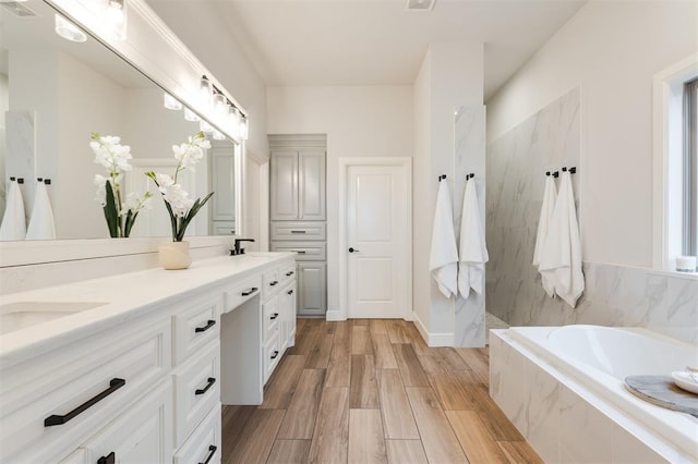 bathroom with a sink, double vanity, wood finished floors, and a bath