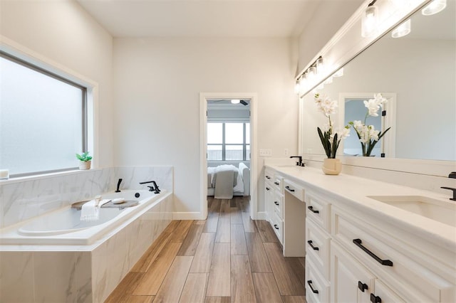 ensuite bathroom featuring double vanity, wood tiled floor, a sink, baseboards, and a bath