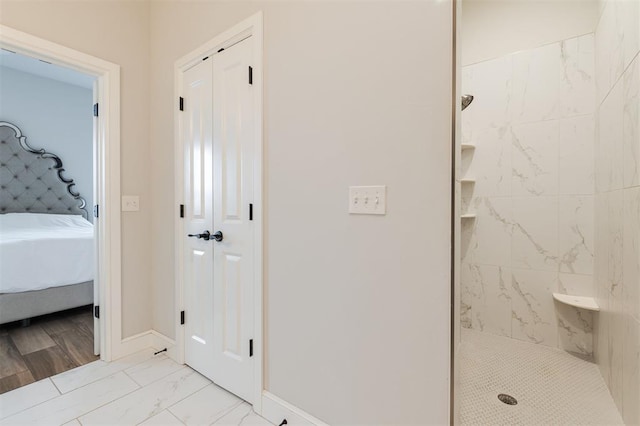 bathroom with ensuite bathroom, marble finish floor, a tile shower, and baseboards