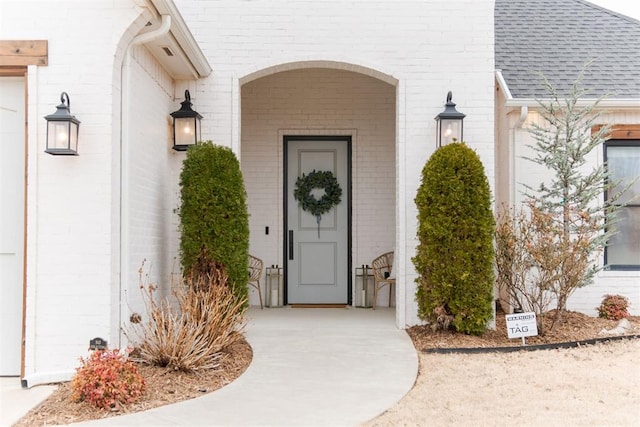 entrance to property with a shingled roof and brick siding