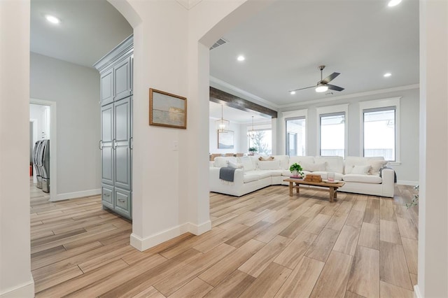 living room with ornamental molding, light wood-type flooring, visible vents, and baseboards